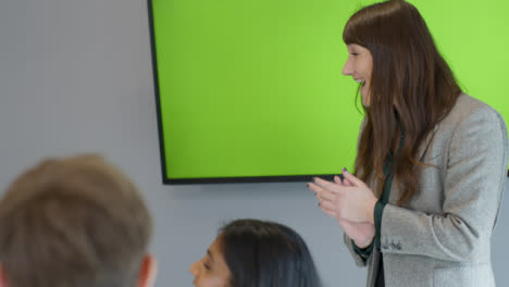 Happy-Businesswoman-Giving-Presentation-To-Colleagues-With-Green-Screen-Tv