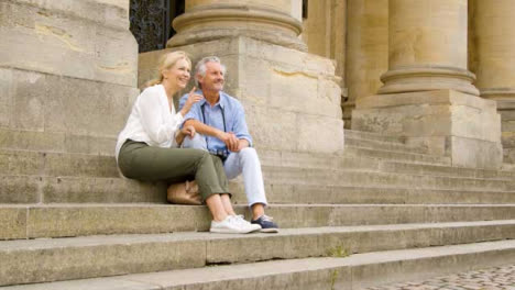 Low-Angle-Shot-of-Middle-Aged-Tourist-Couple-Sitting-On-Old-Steps