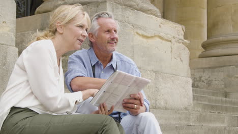 Medium-Shot-of-Middle-Aged-Tourist-Couple-Reading-Map-On-Old-Steps