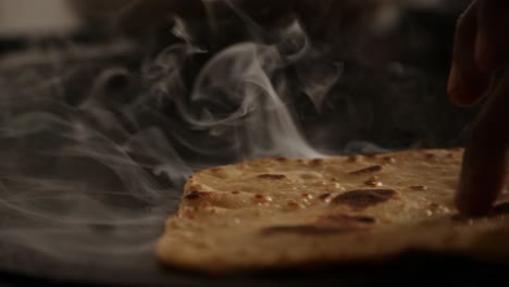 Close-up-of-steaming-hot-roti-cooked-on-a-cast-iron-pan-and-flipping-with-bare-hands