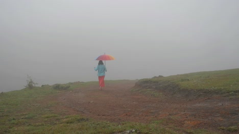 Weitwinkelaufnahme-Einer-Südindischen-Frau,-Die-An-Einem-Nebligen-Morgen-Mit-Einem-Bunten-Regenschirm-Auf-Einem-Hügel-Spaziert?