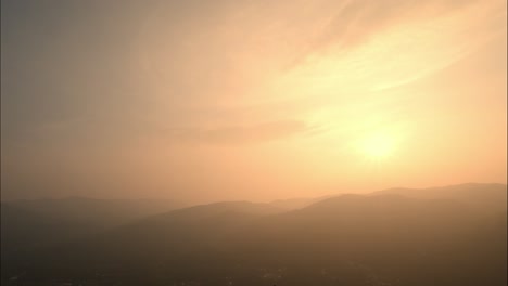 Wide-angle-panning-shot-of-a-beautiful-sunset-over-the-mountains-on-a-hazy-evening-during-golden-hour