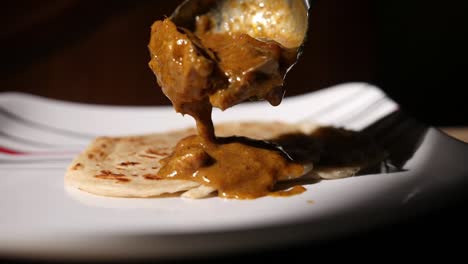 Closeup-dolly-out-dramatic-slow-motion-shot-of-parotta-on-a-plate-with-chicken-curry-being-poured-over-slowly-coming-into-focus