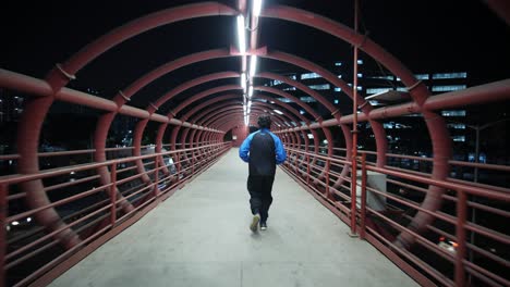 Weitwinkelverfolgung-Eines-Mannes,-Der-In-Den-Frühen-Morgenstunden-Auf-Einem-Metallroten-Skywalk-Joggt