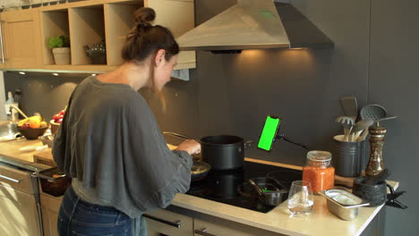 Junge-Frau-Kocht,-Während-Sie-Auf-Den-Grünen-Bildschirm-Des-Telefons-Schaut