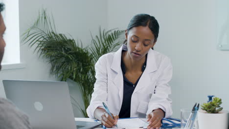 Young-Doctor-Using-Clipboard-Whilst-Talking-to-Patient