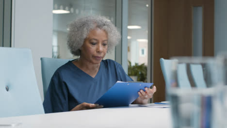 Female-Middle-Aged-Doctor-Looking-at-Notes-In-Office-Space