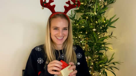 Young-Woman-On-Christmas-Video-Call-Opening-a-Present-Whilst-Talking-to-Camera
