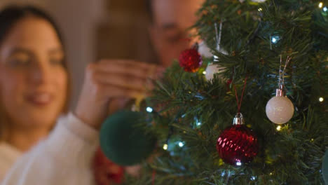 Defokussierte-Aufnahme-Eines-Jungen-Paares,-Das-Zusammen-Den-Weihnachtsbaum-Schmückt