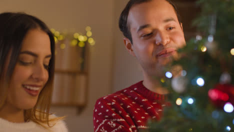 Tracking-Shot-From-Behind-Christmas-Tree-As-Young-Couple-Decorate-It-Together