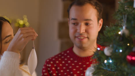 Tracking-Shot-From-Behind-a-Christmas-Tree-As-Young-Couple-Decorate-It-Together