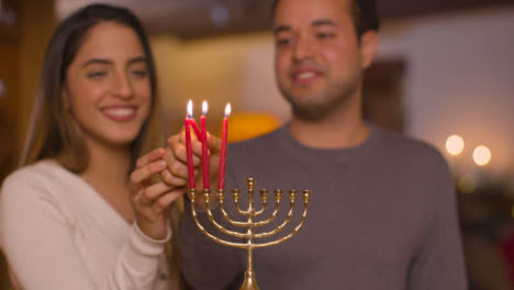 Plano-Medio-De-La-Joven-Pareja-Encendiendo-Tres-Velas-De-Menorá-Durante-Hanukkah