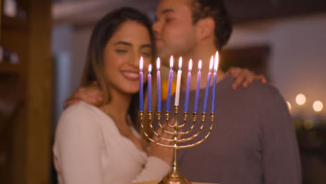 Medium-Shot-of-Young-Couple-Looking-at-Burning-Candles-On-Menorah-During-Hanukkah