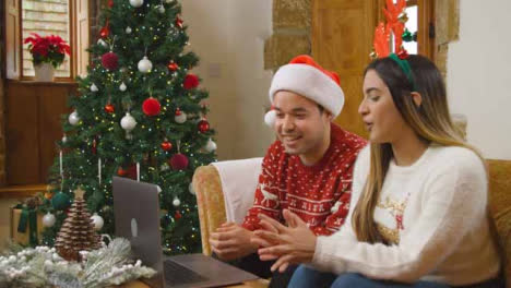 Wide-Shot-of-Young-Couple-Waving-and-Talking-to-Laptop-Camera-During-Christmas-Video-Call-