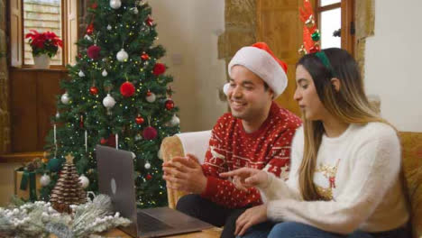 Wide-Shot-of-Young-Couple-Talking-to-Laptop-Camera-During-a-Christmas-Video-Call-