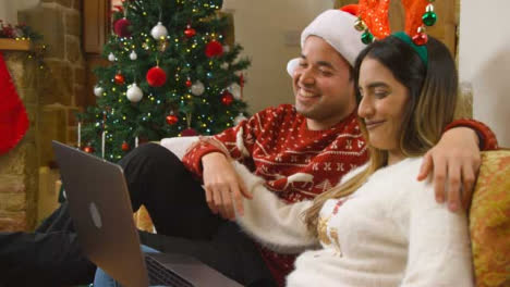 Mittlere-Aufnahme-Eines-Jungen-Paares,-Das-Während-Eines-Weihnachtsvideoanrufs-Mit-Der-Laptopkamera-Spricht