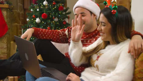Medium-Shot-of-Young-Couple-Waving-and-Talking-to-Laptop-Webcam-During-a-Christmas-Video-Call-
