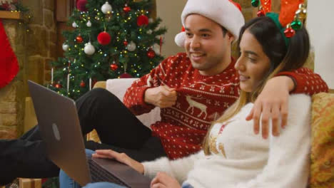 Medium-Shot-of-Young-Couple-Waving-and-Talking-to-Laptop-Camera-During-a-Christmas-Video-Call-