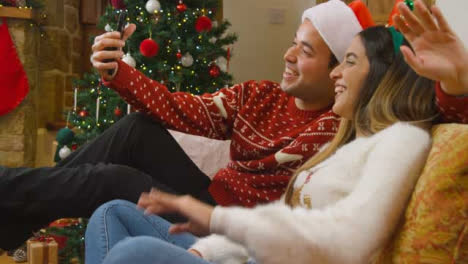 Medium-Shot-of-Young-Couple-Waving-and-Talking-to-Phone-Camera-During-Christmas-Video-Call