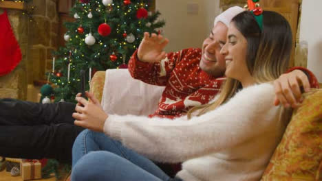 Medium-Shot-of-Young-Couple-Waving-and-Talking-to-Phone-Camera-During-a-Christmas-Video-Call