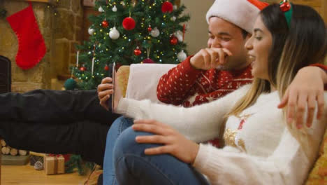 Medium-Shot-of-Young-Couple-Talking-and-Laughing-to-Phone-Camera-During-a-Christmas-Video-Call