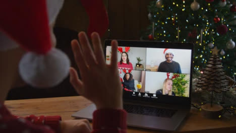 über-Die-Schulter-Geschossen-Von-Einem-Mann,-Der-Winkt-Und-Mit-Freunden-über-Einen-Laptop-Weihnachtsvideoanruf-Spricht-Talking