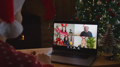 Over-the-Shoulder-Shot-of-Man-Waving-and-Talking-to-Friends-Via-Laptop-Christmas-Video-Call