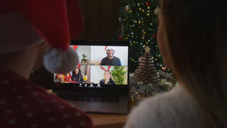Over-the-Shoulder-Shot-of-Couple-Waving-and-Talking-to-Friends-Via-Laptop-Christmas-Video-Call