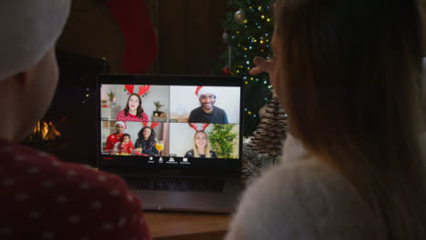über-Die-Schulter-Geschossen-Von-Einem-Paar,-Das-Mit-Freunden-über-Einen-Laptop-Weihnachtsvideoanruf-Spricht-Talking