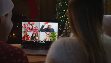 Over-the-Shoulder-Shot-of-Couple-Waving-and-Talking-to-Friends-On-Laptop-Christmas-Video-Call