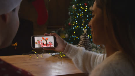 Over-the-Shoulder-Shot-of-Couple-Talking-to-Friend-On-Mobile-Phone-Christmas-Video-Call