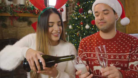 Junges-Paar-öffnet-Eine-Flasche-Champagner-Während-Des-Weihnachtsvideoanrufs