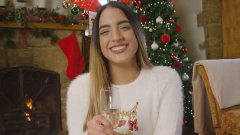 Young-Woman-Holding-Glass-of-Champagne-and-Talking-to-Camera-During-Christmas-Video-Call