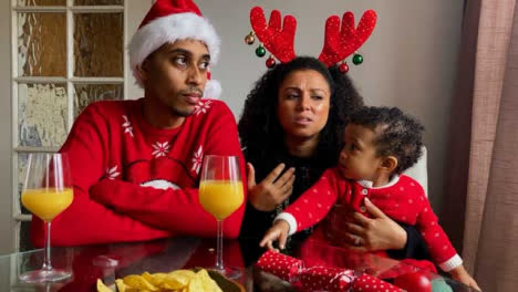 Young-Parents-with-Small-Child-On-Christmas-Video-Call-Listening-and-Talking-to-Camera