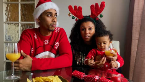 Young-Parents-with-Small-Child-On-a-Christmas-Video-Call-Listening-and-Talking-to-Camera