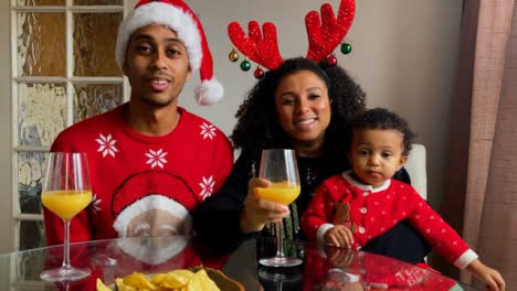 Young-Parents-with-Small-Niño-On-Christmas-Video-Call-Celebrating-and-Raising-Glasses-to-Camera