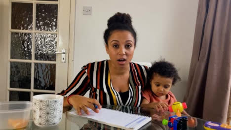 Young-Woman-with-Small-Child-On-Business-Video-Call-Briefing-Others-Whilst-Looking-Directly-to-Camera