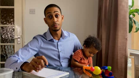Young-Man-with-Small-Child-On-Business-Video-Call-Briefing-Others-Whilst-Looking-Directly-to-Camera