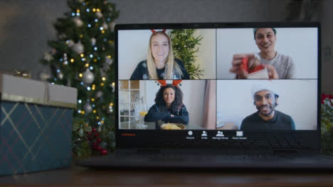 Sliding-Close-Up-Shot-of-a-4-Way-Split-Screen-Christmas-Themed-Group-Video-Call-On-Laptop-Amongst-Friends
