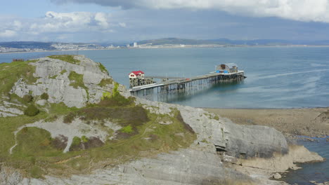 Drone-Shot-Flying-Past-Cliff-Concealing-Mumbles-Pier-In-Swansea