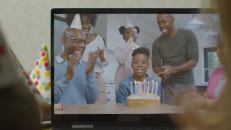 Sliding-Over-the-Shoulder-Shot-of-Laptop-Screen-with-Family-Singing-Happy-Birthday-On-Video-Call