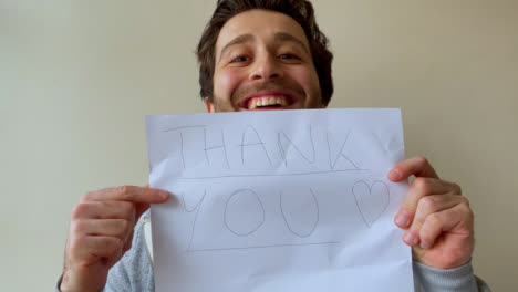 Young-Male-University-Student-Holding-Up-Thank-You-Sign-During-Video-Lecture