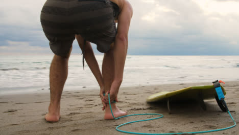 Tracking-Shot-of-Young-Surfer-Tieing-Surfboard-Leash-and-Walking-Towards-Waves