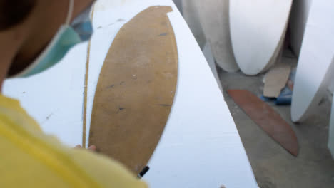 Handheld-Over-the-Shoulder-Shot-of-Surfboard-Shaper-Tracing-Onto-Polystyrene-Board