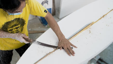 Handheld-High-Angle-Shot-of-Surfboard-Shaper-Cutting-Wood-Away-from-Polystyrene-Board