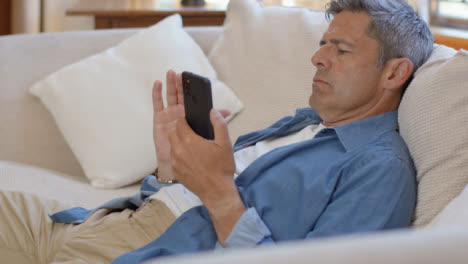 Mittlere-Aufnahme-Eines-Mannes-Mittleren-Alters,-Der-Mit-Smartphone-Auf-Dem-Sofa-Ruht