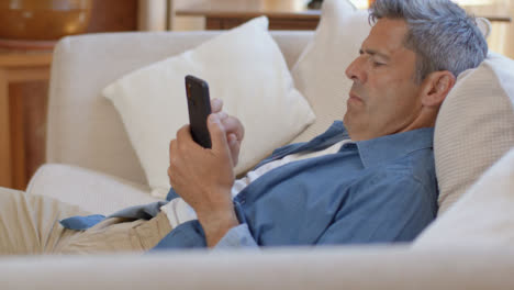 Tilting-Shot-of-Middle-Aged-Man-Slouched-On-Sofa-Using-Smartphone-