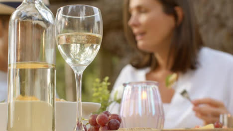 Nahaufnahme-Einer-Weinflasche-Und-Eines-Glases-Mit-Einem-Paar,-Das-Im-Hintergrund-Ein-Abendessen-Im-Freien-Genießt?