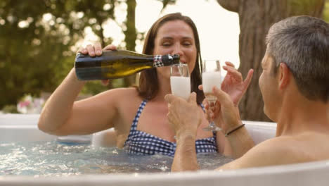 Over-the-Shoulder-Shot-of-Middle-Aged-Couple-Pouring-Champagne-in-Hot-Tub