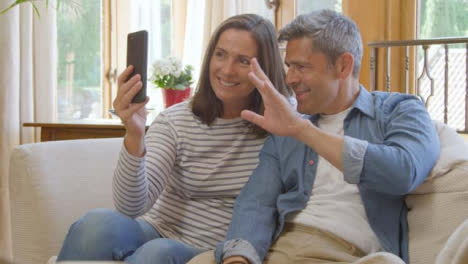 Sliding-Shot-of-Middle-Aged-Couple-Waving-Goodbye-into-Smartphone-During-Video-Call